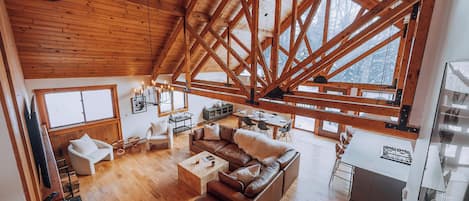 Un loft espacioso con techo alto y vigas de madera a la vista, que cuenta con una zona de estar acogedora con un sofá de cuero, una mesa de comedor y una cocina.