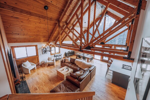 A spacious loft with a high ceiling and exposed wooden beams, featuring a cozy living area with a leather sofa, a dining table, and a kitchen area. - Designer 4-bedroom house in charming Stratton home sleeps 16 (Stratton)