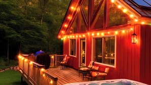 Eine Holzterrasse mit Whirlpool und überdachter Sitzgelegenheit, umgeben von einer Terrasse mit Lichterketten.