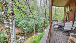 A wooden deck with outdoor furniture overlooking a forested area with a stream. - Rushing Waters Cabin (Sylva)