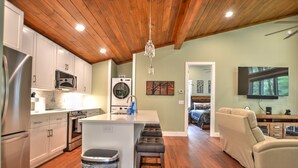A modern kitchen with wooden ceiling, stainless steel appliances, and a central island with stools. - Rushing Waters Cabin (Sylva)