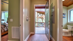 A hallway with a wooden floor, a door leading to a balcony, and a visible toilet. - Rushing Waters Cabin (Sylva)