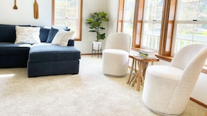 Uma sala de estar com um sofá modular azul escuro, uma poltrona branca, uma pequena mesa de madeira com livros e um vaso de planta.