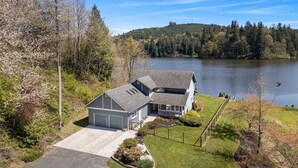 Uma casa de dois andares com garagem, varanda coberta e vista para um lago.