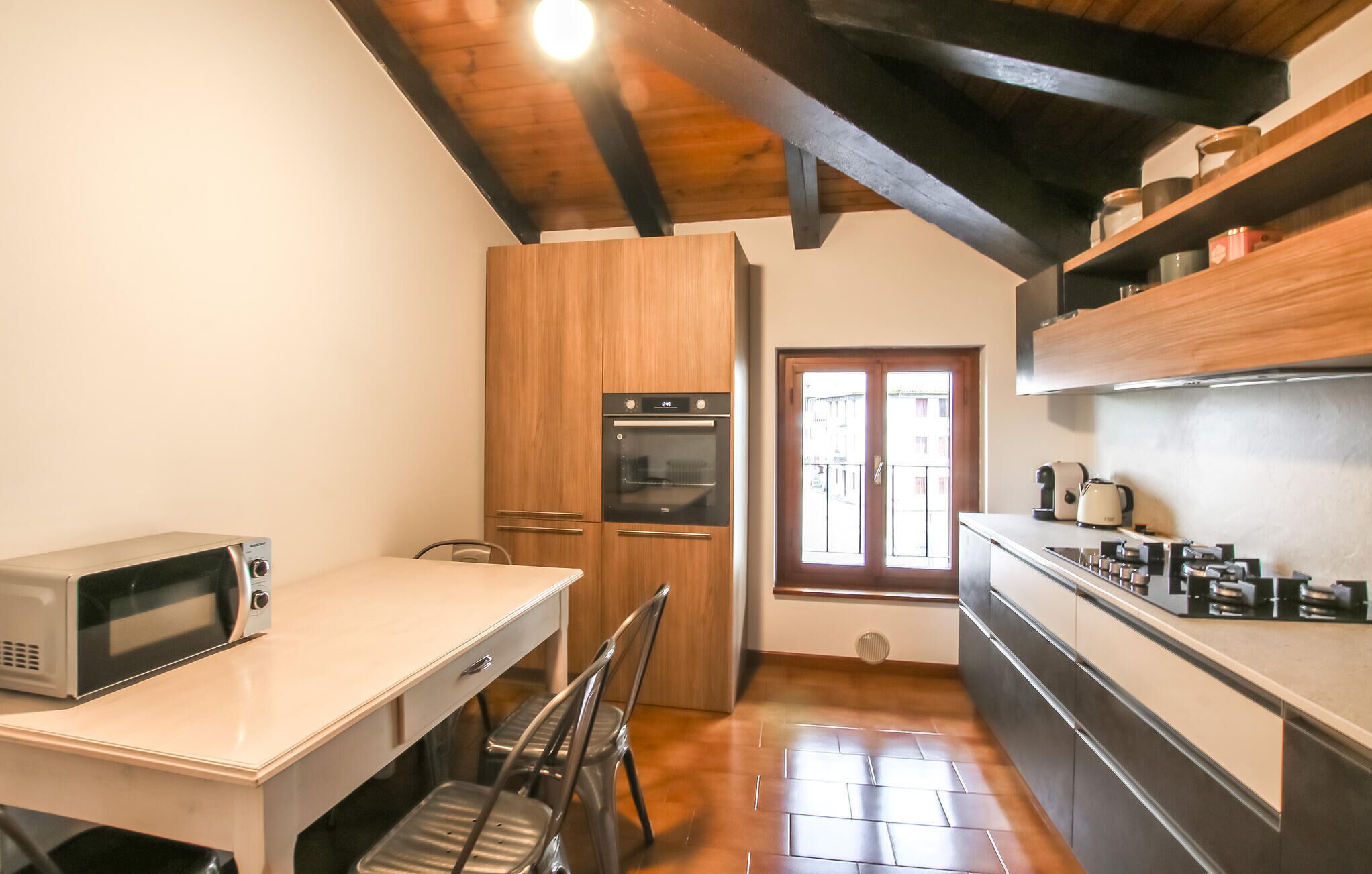 A compact kitchen with a microwave, oven, and a dining area with a chair.