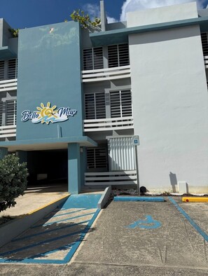 Um edifício com uma placa indicando 'Bella Mar' e uma área de estacionamento com linhas azuis e o símbolo de acessibilidade para cadeirantes.
