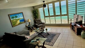 A living room with a large window overlooking the ocean, a comfortable sofa, a coffee table, and a television.