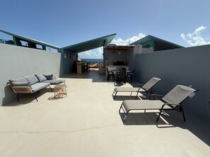 Um terraço no telhado com um sofá, cadeiras de lounge e uma área de refeições com churrasqueira.