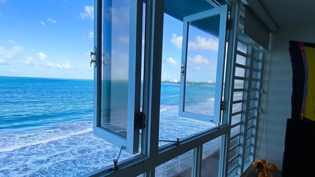 A room with large windows overlooking a beach with waves.