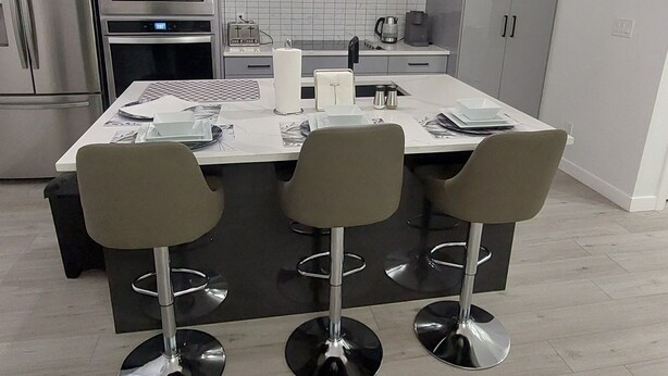 A modern kitchen with a central island, stainless steel appliances, and three bar stools.