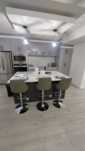 Una cocina moderna con una isla central, electrodomésticos de acero inoxidable y tres taburetes de bar.