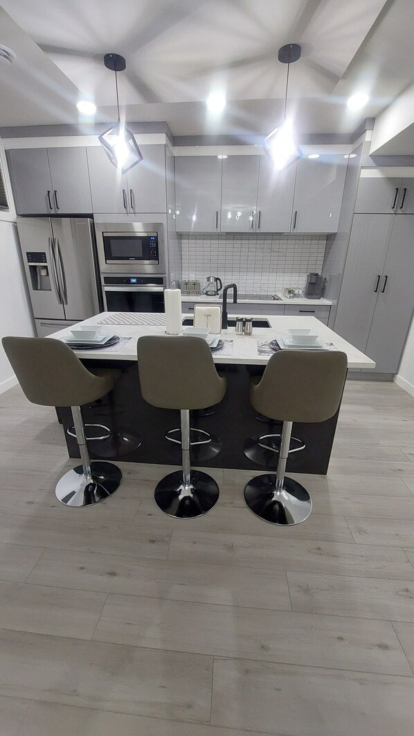 A modern kitchen with a central island, bar stools, stainless steel appliances, and pendant lighting.
