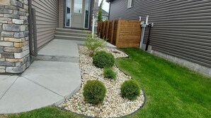 A modern two-story house with a stone foundation, a well-maintained lawn, and a wooden fence.