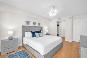 Un dormitorio moderno con una cama, mesitas de noche, un ventilador de techo y obras de arte en la pared.