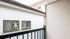 Un edificio blanco con dos ventanas que presentan patrones geométricos, una barandilla negra y una puerta parcialmente visible.