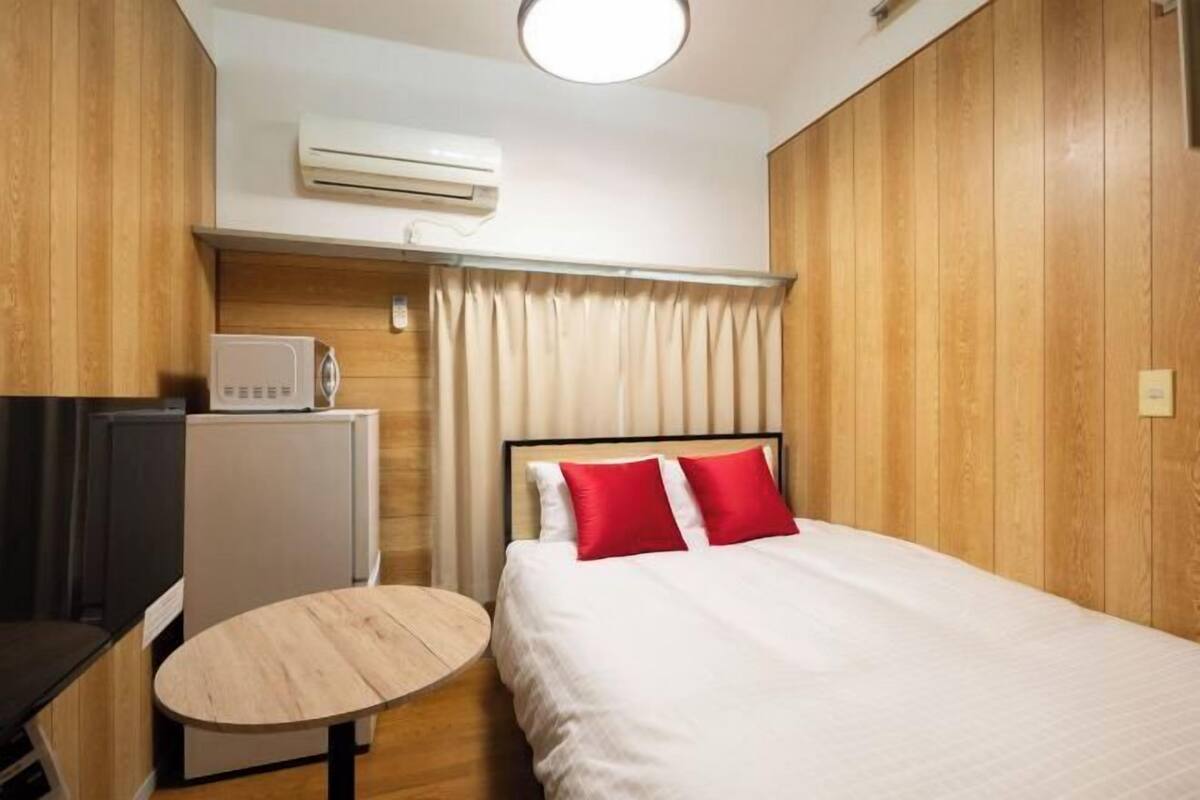 Une chambre d’hôtel de taille réduite, comprenant un lit, une petite table, un téléviseur et un appareil de climatisation.