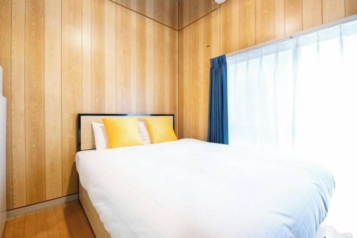 Une chambre avec un mur lambrissé en bois, un lit avec une literie blanche et deux oreillers, et une fenêtre avec des rideaux bleus.