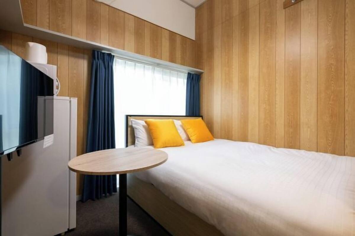 Une chambre d’hôtel avec un lit, une petite table, un réfrigérateur et des panneaux de bois aux murs.