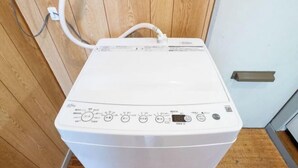 Una lavadora blanca con panel de control, cable de alimentación y un asa fijada a la pared.