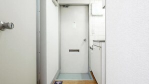 Un pasillo estrecho con una puerta blanca, un escalón pequeño y un felpudo en el suelo.