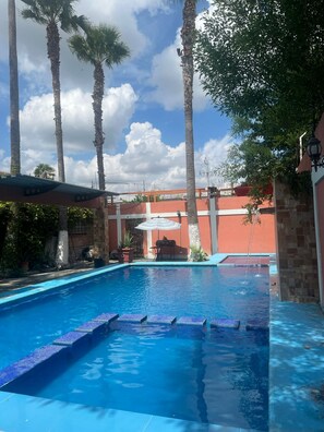 Piscina com água azul cristalina, rodeada por palmeiras e um muro de pedra.