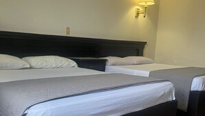 Quarto de hotel com duas camas, uma cabeceira escura, uma luminária de parede e piso de azulejos.