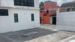 Uma área de estacionamento com um carro branco, um edifício com grandes janelas e um edifício vermelho ao fundo.
