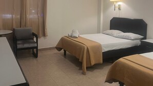 Quarto de hotel com duas camas, uma cadeira, uma escrivaninha, ar condicionado e uma luminária na parede.