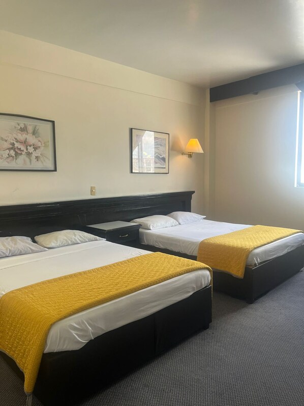 A hotel room with two beds, a dark headboard, a wall-mounted lamp, and a window.