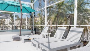 A sunlit outdoor lounge area with white lounge chairs, a small table, and a teal umbrella. - Magic Retreat Orlando (Davenport)