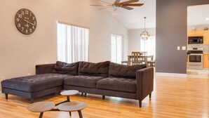 A modern living room with a sectional sofa, a round clock, and a dining area with a chandelier. - Magic Retreat Orlando (Davenport)