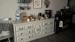 Une cuisine avec des meubles blancs, une machine à café et un four à micro-ondes posés sur le plan de travail.