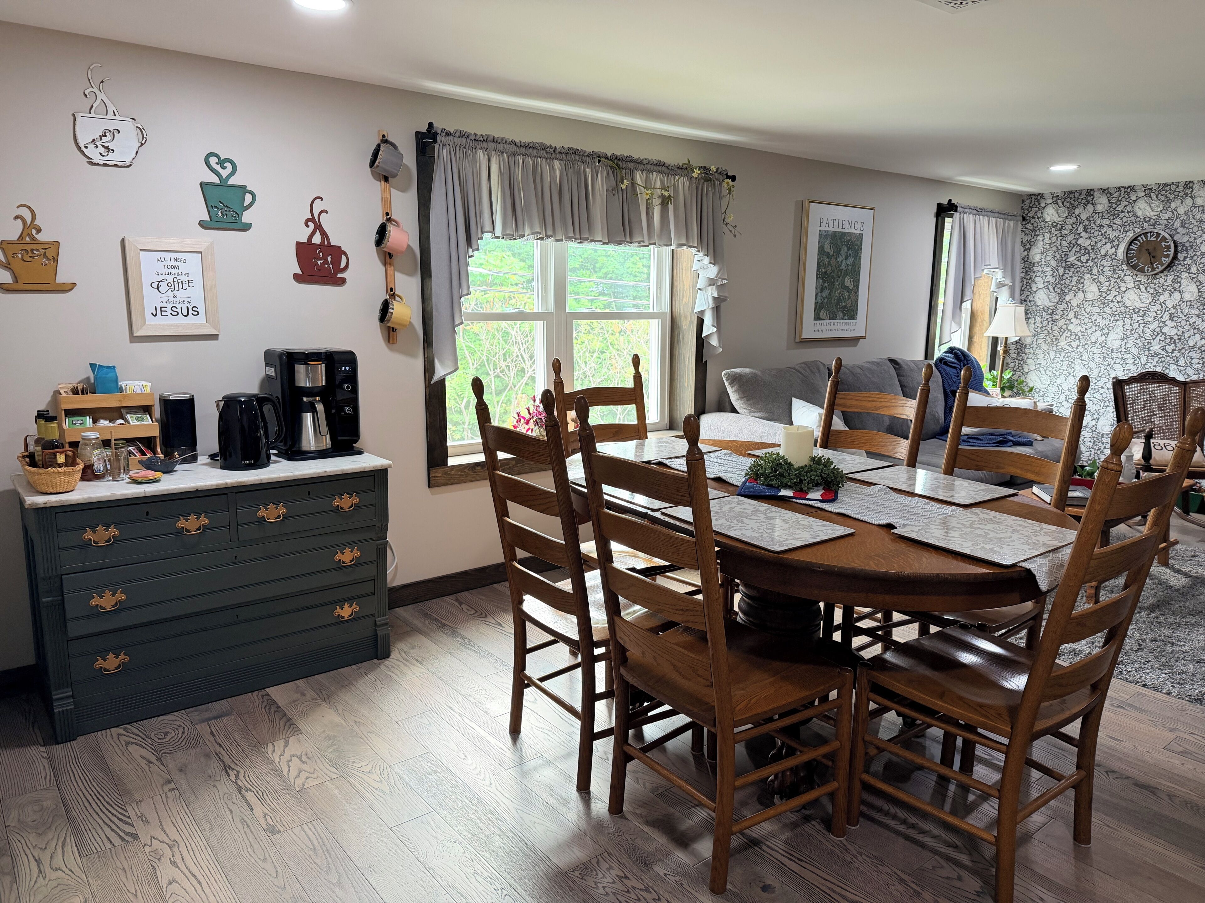 Área de refeições com mesa e cadeiras de madeira, um canto para café e vista para o exterior.