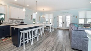 Una cocina moderna con armarios blancos, una isla central con taburetes y un comedor con mesa y sillas.