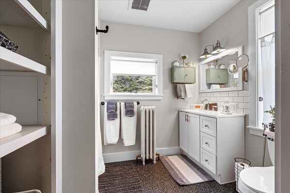 A bathroom with a window, a radiator, a sink with a mirror, and a towel rack. - 79th on Main: Restored Barn in the Finger Lakes (Trumansburg)