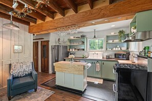 A kitchen with wooden beams, a central island, a refrigerator, a sink, and a stove. - 79th on Main: Restored Barn in the Finger Lakes (Trumansburg)