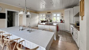 Une cuisine spacieuse dotée d’un grand îlot central, de meubles blancs et d’un coin repas avec une longue table et des chaises.