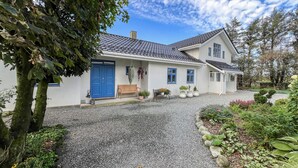 Une maison à deux étages avec une allée en gravier, une porte bleue et un banc à l’extérieur.
