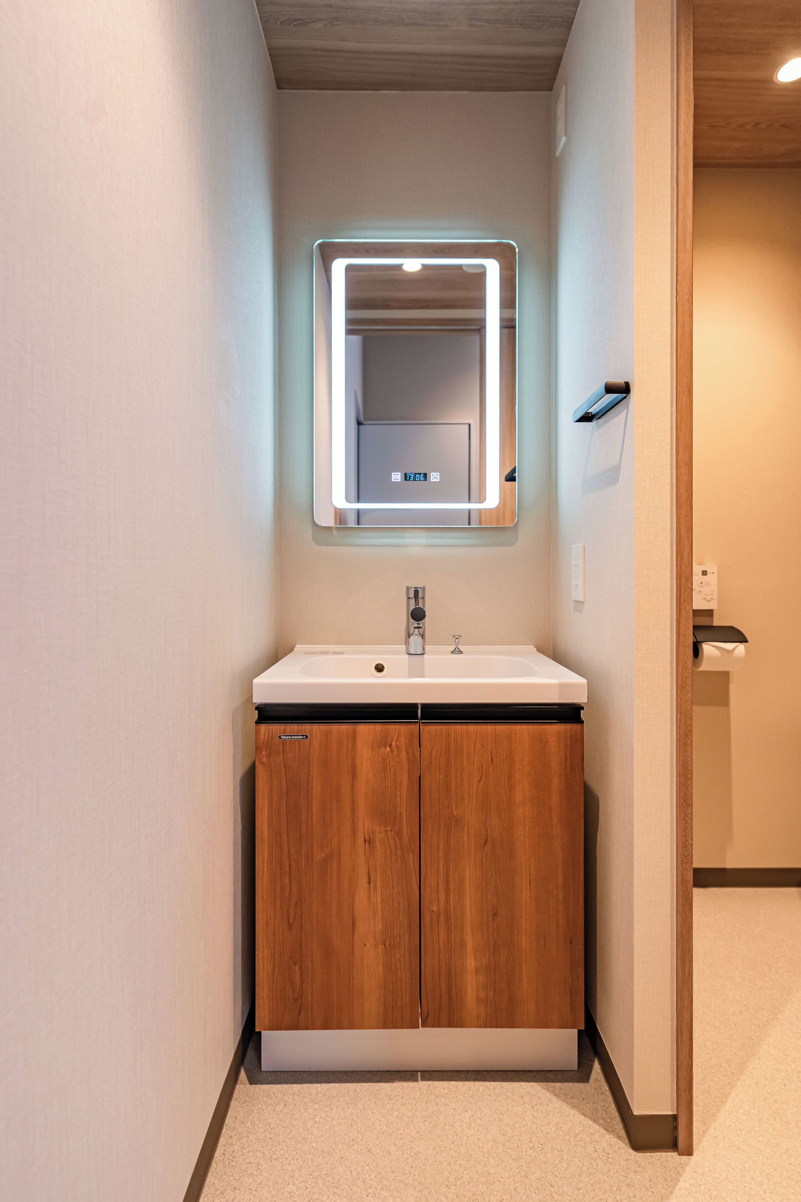 A bathroom with a wooden vanity, a white sink, and a mirror with built-in lighting.