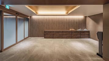 A modern lobby with a wooden reception desk, a glass partition, and a tiled floor.