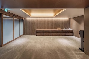 A modern lobby with a wooden reception desk, a glass partition, and a tiled floor.