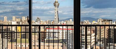 Vista desde una ventana con baranda metálica, que da a un paisaje urbano con edificios y una torre.
