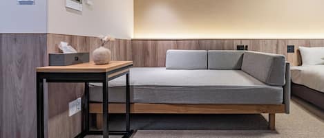 Un dormitorio moderno con diseño minimalista, que incluye una cama, una mesita de noche y un escritorio pequeño con una lámpara.