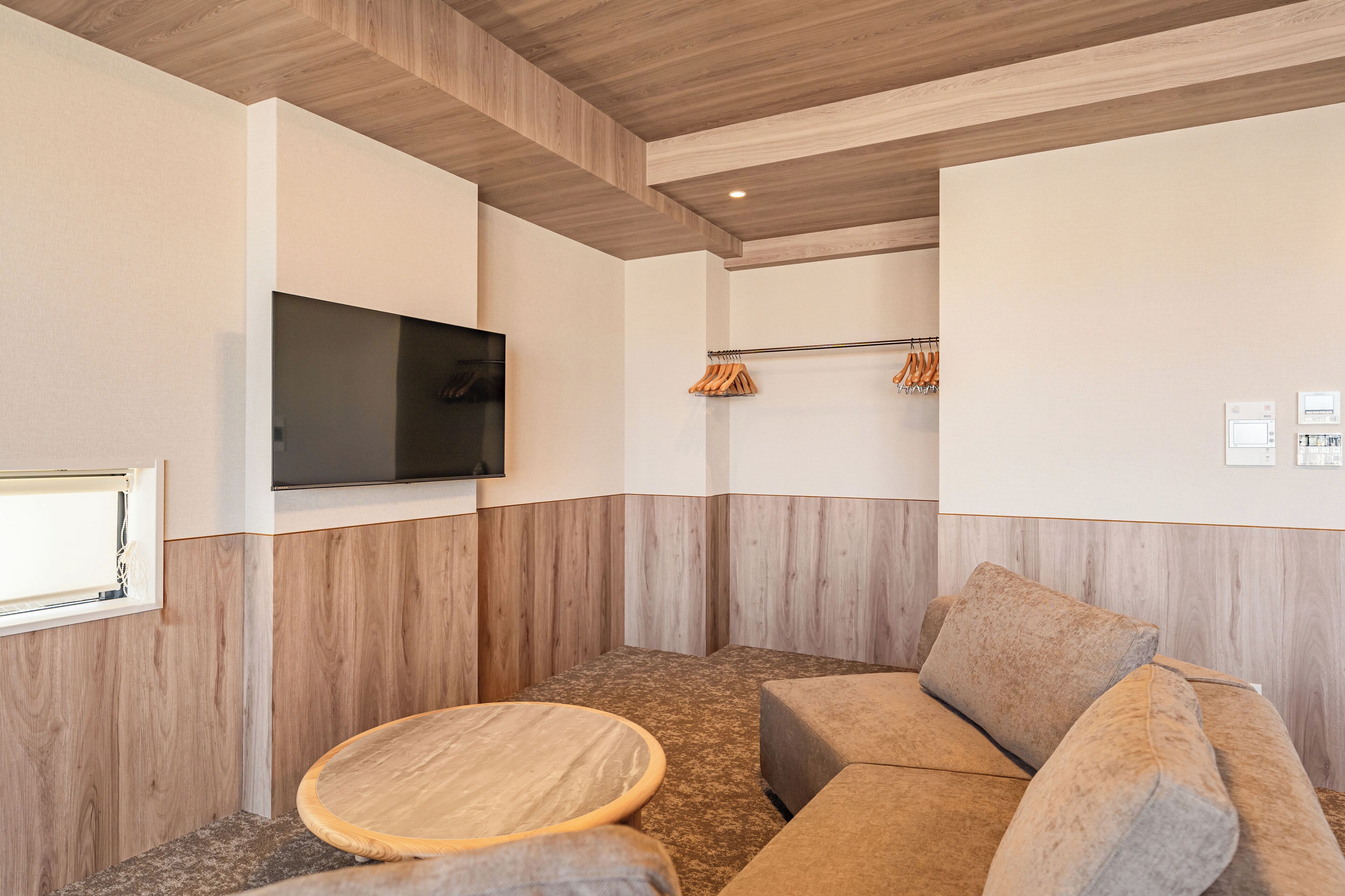 A modern room with a wooden ceiling, a flat-screen TV mounted on the wall, a sofa, and a round wooden table.