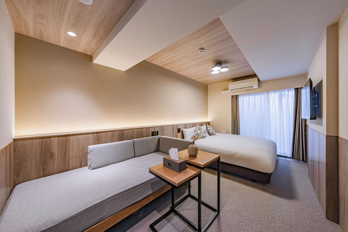 A modern hotel room with a sofa, a small table, a bed, and a TV.