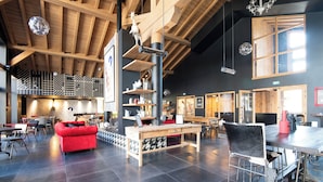 A spacious indoor area with a high ceiling, wooden beams, and a central table with chairs. - Appartement Havre des Alpes - Welkeys (Megève)
