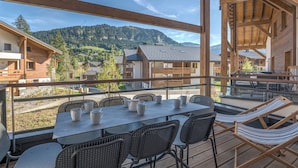 A wooden deck with a table and chairs, overlooking a mountainous landscape. - Appartement Havre des Alpes - Welkeys (Megève)