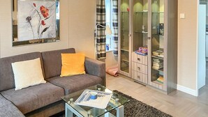 Un salón con un sofá gris, una mesa de centro de vidrio y un cuadro en la pared.