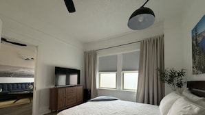A bedroom with a bed, a TV, a dresser, and a window with curtains.