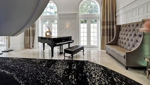 Un vaste espace de vie agrémenté d’un magnifique piano à queue, d’un canapé confortable et d’une grande fenêtre ornée de rideaux.